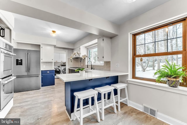 kitchen featuring a breakfast bar, appliances with stainless steel finishes, washing machine and dryer, white cabinets, and kitchen peninsula