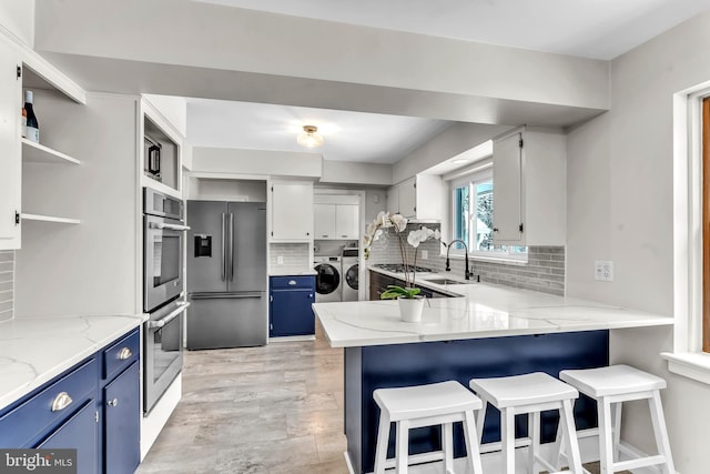 kitchen with blue cabinetry, appliances with stainless steel finishes, light stone counters, washer and dryer, and white cabinets