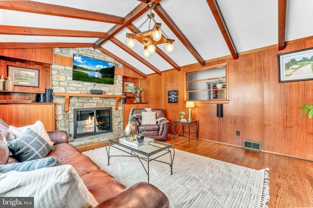 living room with vaulted ceiling with beams, a stone fireplace, light hardwood / wood-style flooring, and wood walls