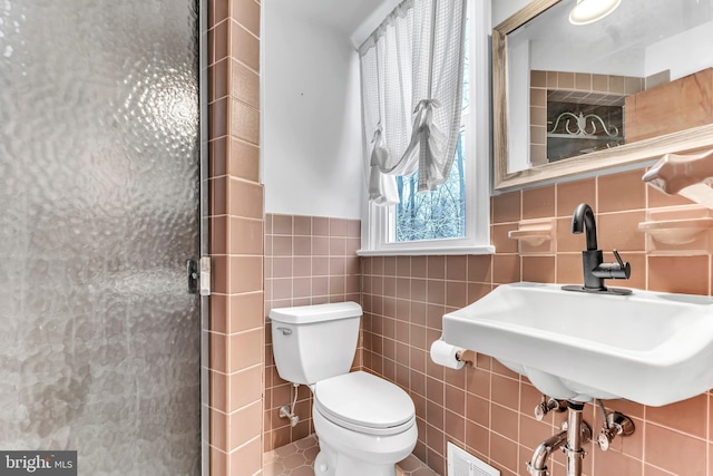 bathroom featuring a shower with door, sink, tile walls, and toilet