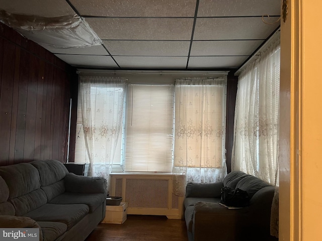 interior space with wood walls, radiator heating unit, wood-type flooring, and a drop ceiling