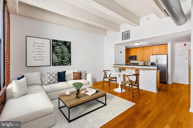 living area featuring visible vents, baseboards, beamed ceiling, and light wood-style flooring