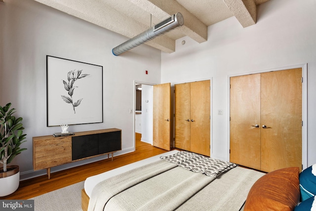 bedroom with beam ceiling, two closets, a high ceiling, and wood finished floors