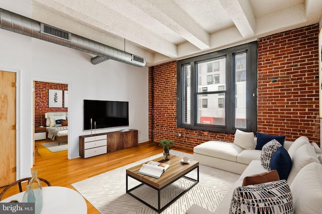 living room with visible vents, beam ceiling, a textured ceiling, wood finished floors, and brick wall