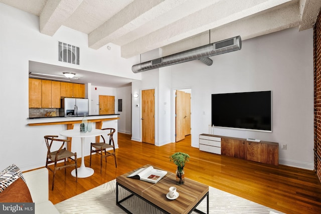 living room with beam ceiling, wood finished floors, visible vents, and baseboards