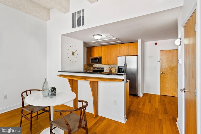 kitchen featuring wood finished floors, visible vents, a peninsula, decorative backsplash, and appliances with stainless steel finishes