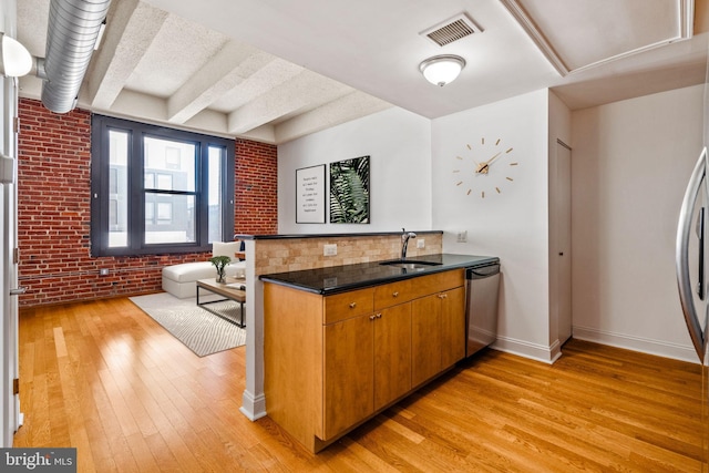 kitchen featuring light wood-style floors, visible vents, stainless steel dishwasher, and brick wall