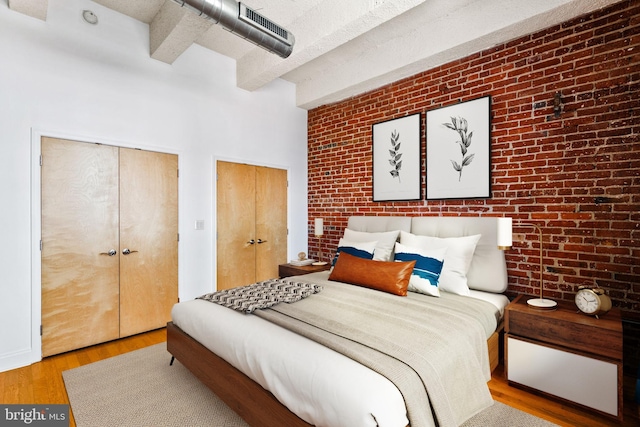 bedroom featuring beamed ceiling, brick wall, two closets, and wood finished floors