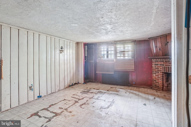 unfurnished room featuring wooden walls, radiator heating unit, a fireplace, and a textured ceiling