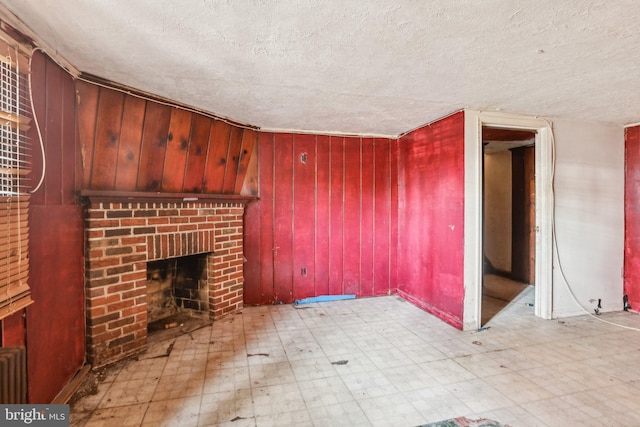 unfurnished living room with wooden walls, a brick fireplace, and a textured ceiling