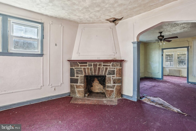 unfurnished living room featuring ceiling fan, a stone fireplace, radiator, and a textured ceiling