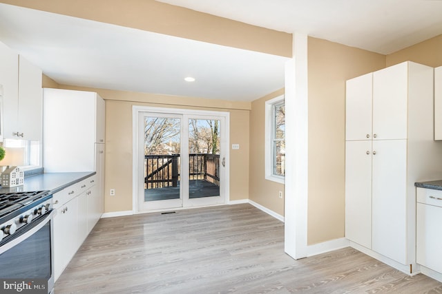 kitchen with light hardwood / wood-style flooring, stainless steel gas range oven, and white cabinets