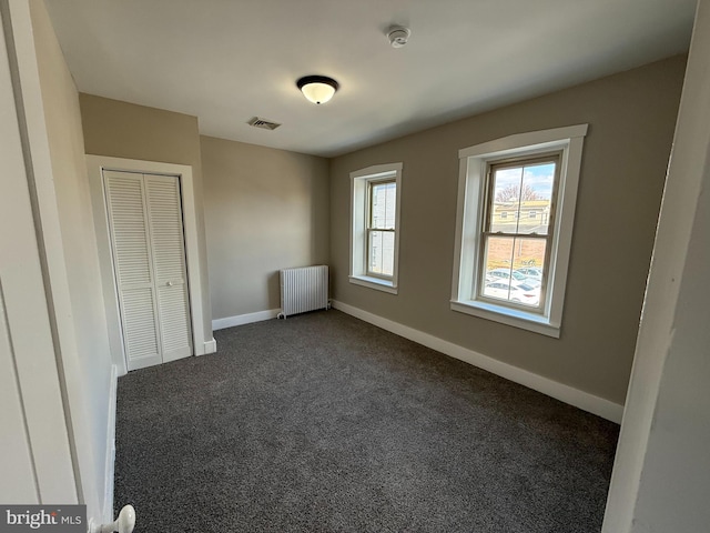 unfurnished bedroom with radiator, dark carpet, and a closet