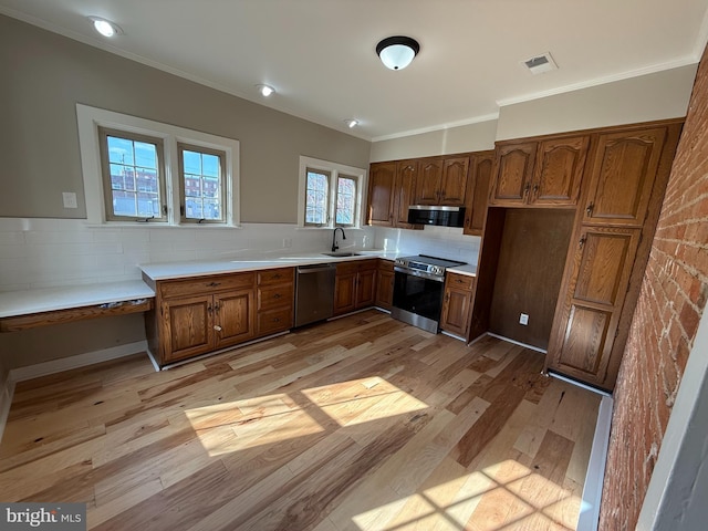 kitchen with tasteful backsplash, sink, ornamental molding, stainless steel appliances, and light hardwood / wood-style flooring