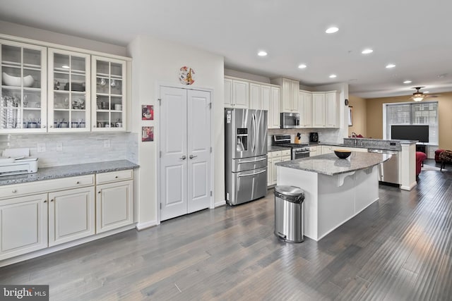 kitchen with appliances with stainless steel finishes, a kitchen island, a kitchen breakfast bar, dark hardwood / wood-style floors, and light stone countertops