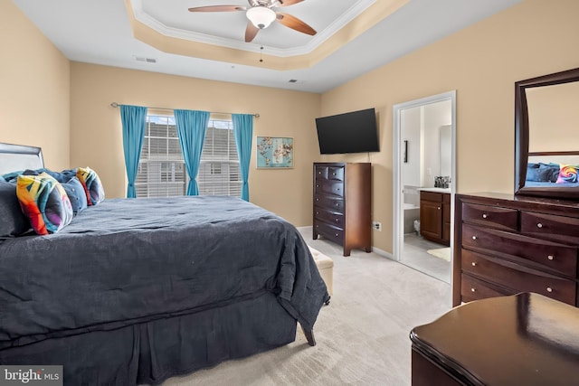 bedroom with ornamental molding, a raised ceiling, light colored carpet, and ensuite bath