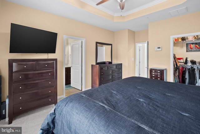 bedroom featuring a closet, a walk in closet, a tray ceiling, crown molding, and light colored carpet