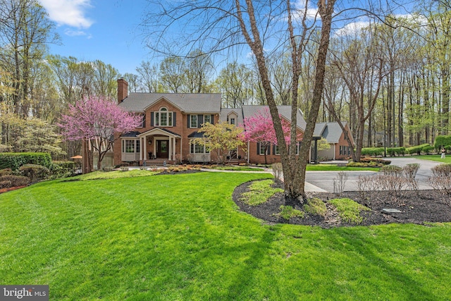 view of front of property featuring a chimney, brick siding, and a front yard