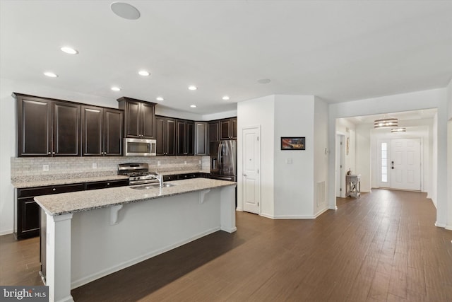 kitchen with sink, a breakfast bar area, light stone counters, stainless steel appliances, and a kitchen island with sink