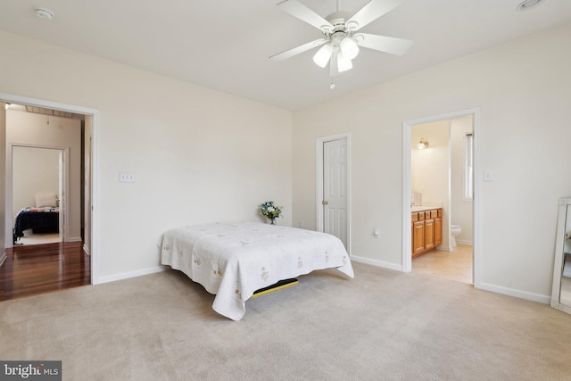 bedroom featuring light carpet, ceiling fan, ensuite bath, and baseboards