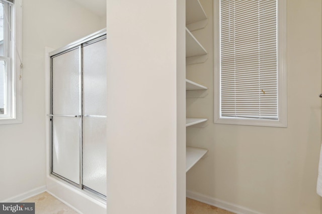 bathroom with a shower with door and baseboards