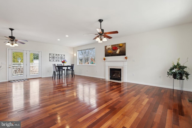 unfurnished living room with wood-type flooring, baseboards, ceiling fan, and a fireplace with flush hearth