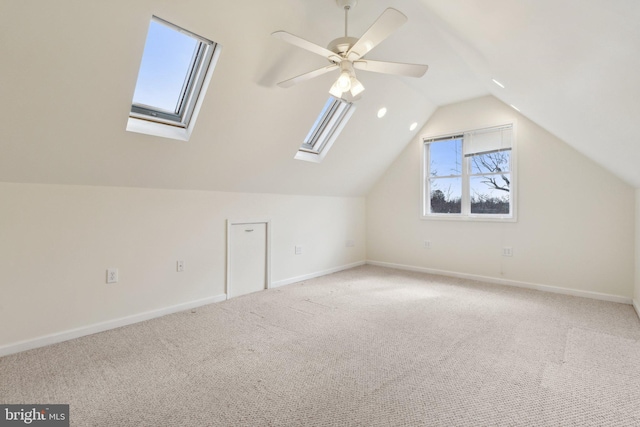 additional living space featuring carpet floors, vaulted ceiling with skylight, baseboards, and ceiling fan