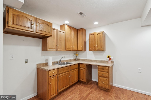 kitchen with visible vents, a sink, light wood-style flooring, and baseboards