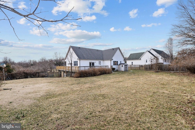 back of house featuring a storage unit, a lawn, a fenced backyard, an outdoor structure, and a wooden deck