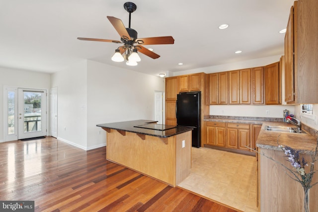 kitchen with light wood-style floors, a center island, black appliances, a kitchen bar, and a sink