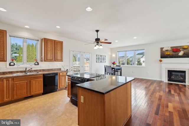 kitchen featuring a center island, brown cabinets, a glass covered fireplace, a sink, and black appliances