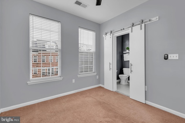 unfurnished bedroom featuring ceiling fan, carpet flooring, connected bathroom, and a barn door