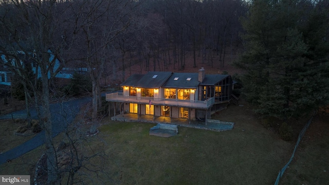 back house at night featuring a lawn and a deck