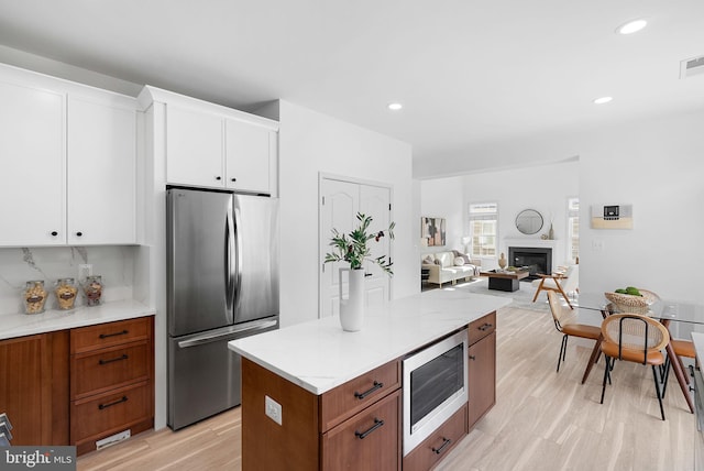 kitchen featuring light countertops, appliances with stainless steel finishes, a glass covered fireplace, open floor plan, and white cabinetry