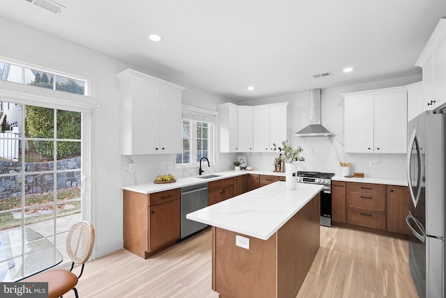 kitchen featuring a center island, appliances with stainless steel finishes, white cabinetry, a sink, and wall chimney exhaust hood