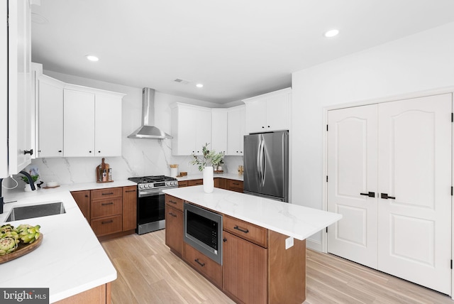 kitchen with a sink, a kitchen island, white cabinets, appliances with stainless steel finishes, and wall chimney exhaust hood