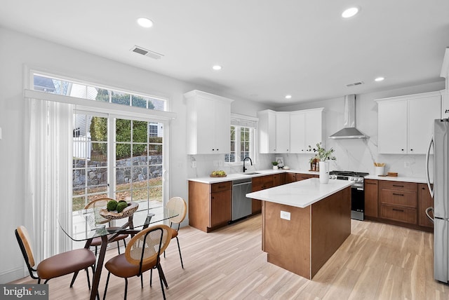 kitchen featuring stainless steel appliances, visible vents, light countertops, a center island, and wall chimney exhaust hood