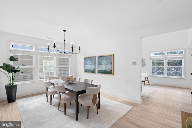 dining space with a wealth of natural light, light wood-style flooring, baseboards, and an inviting chandelier