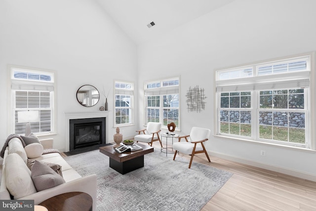 living room with baseboards, plenty of natural light, a fireplace with flush hearth, and light wood-style floors