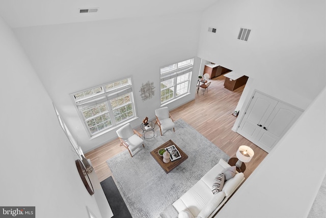 living room with a wealth of natural light, visible vents, light wood-style flooring, and a high ceiling