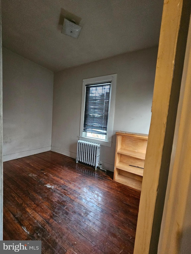 empty room featuring radiator heating unit and dark hardwood / wood-style flooring