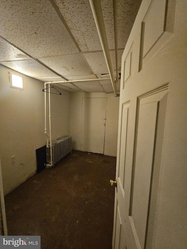 basement with a paneled ceiling and radiator heating unit