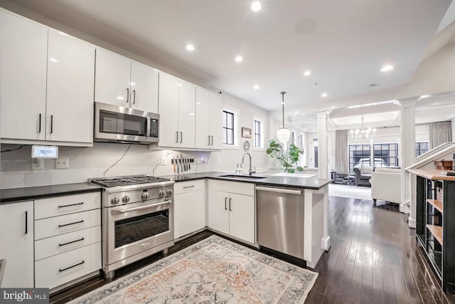 kitchen with sink, white cabinetry, hanging light fixtures, appliances with stainless steel finishes, and decorative columns