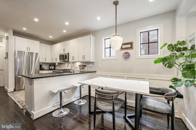 kitchen featuring dark hardwood / wood-style floors, stainless steel appliances, decorative light fixtures, and white cabinets