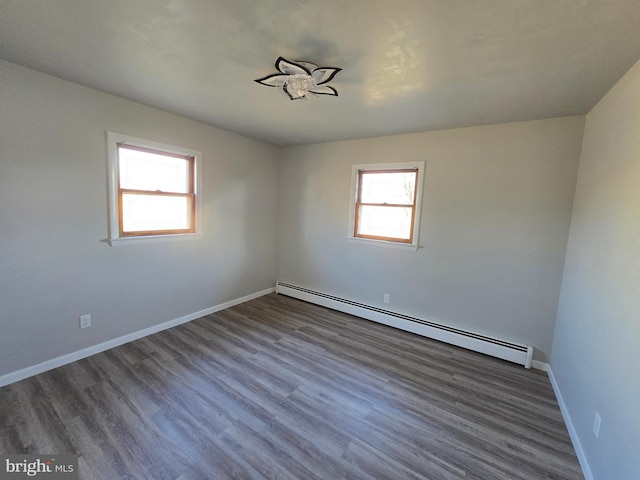 empty room with dark hardwood / wood-style floors, a wealth of natural light, and a baseboard heating unit