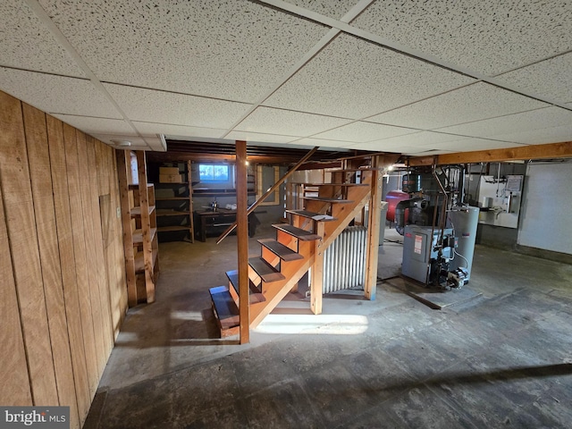 basement with gas water heater, a paneled ceiling, and wooden walls