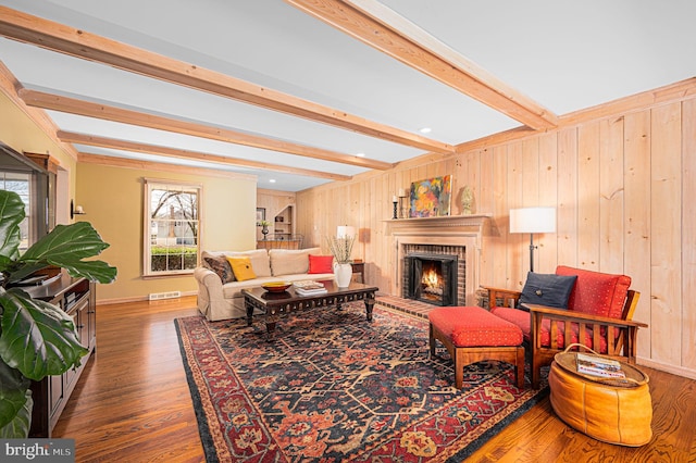 living room with a fireplace, beamed ceiling, wooden walls, and wood finished floors