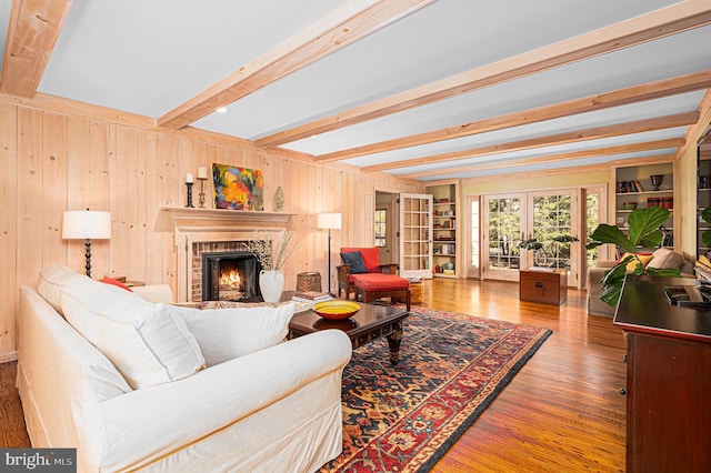 living area with a brick fireplace, wood finished floors, beamed ceiling, french doors, and wood walls