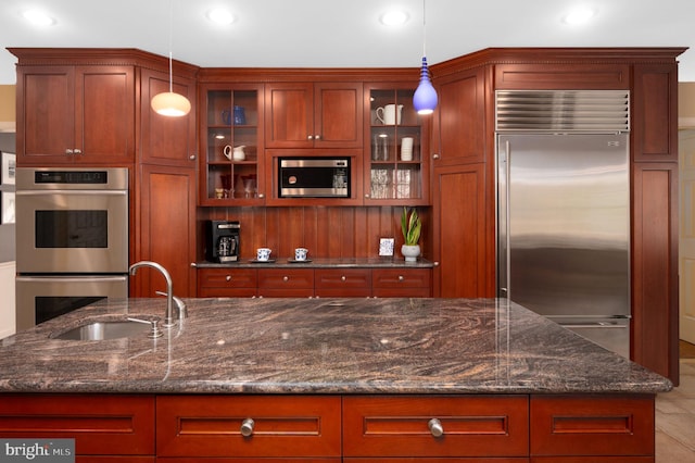 kitchen with glass insert cabinets, pendant lighting, a sink, and built in appliances