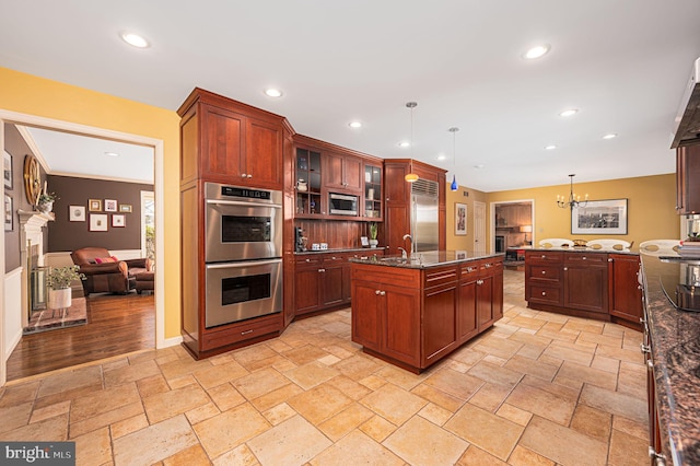 kitchen featuring glass insert cabinets, built in appliances, hanging light fixtures, stone tile flooring, and recessed lighting